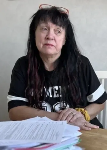 Susanna Lindh sitter vid ett bord med en stor hög papper framför sig i ett ljust rum. En grön växt syns i förgrunden.