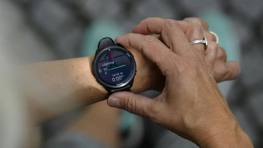En person justerar en träningsklocka på sin handled. Skärmen visar data som pulsmätning, vilket symboliserar användning av wearables för att optimera hälsa och träning.