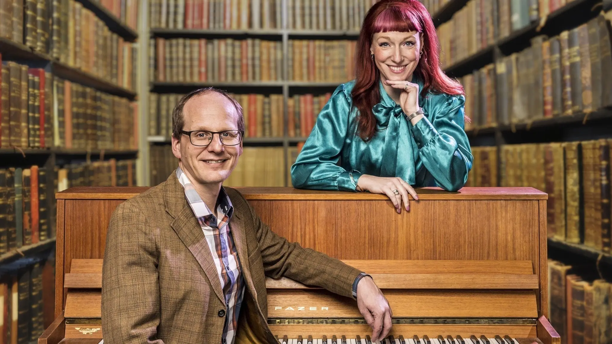 Musikprofessorn Mattias Lundberg sitter vid ett piano. Josefin Johansson står bakom pianot. Båda ler.
