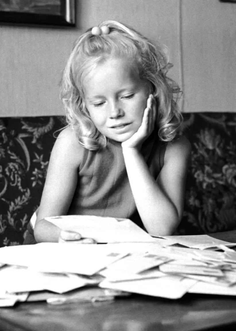 En ung Anita Hegerland sitter i en soffa och sneglar ner mot ett bord där det ligger massa brev från fansen i Sverige. Man ser tavlor på väggen i bakgrunden och på bordet står också en bukett med blommor i en vas. 