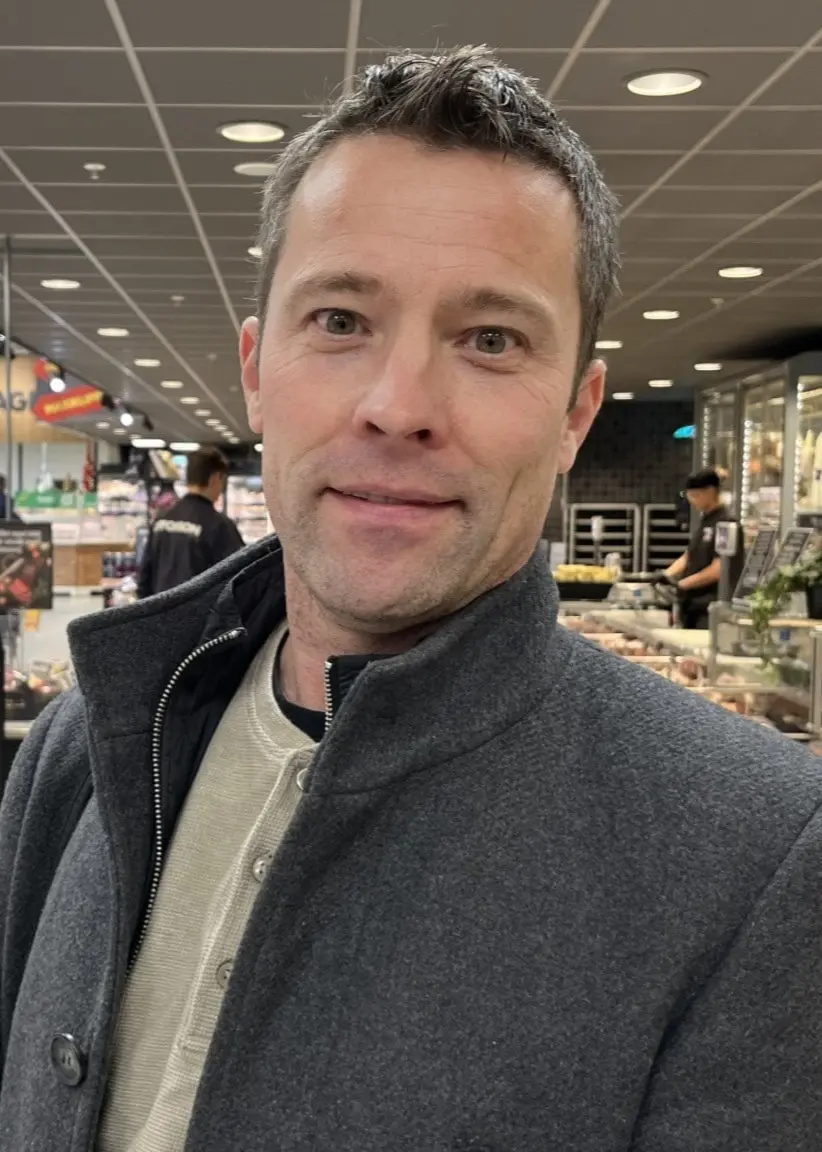 En man med grå kappa står inomhus i en livsmedelsbutik. Bakom honom syns butikshyllor med matvaror och flera kunder i rörelse. Johans drag i ansjoviskrisen – så stoppar butiken bunkringen