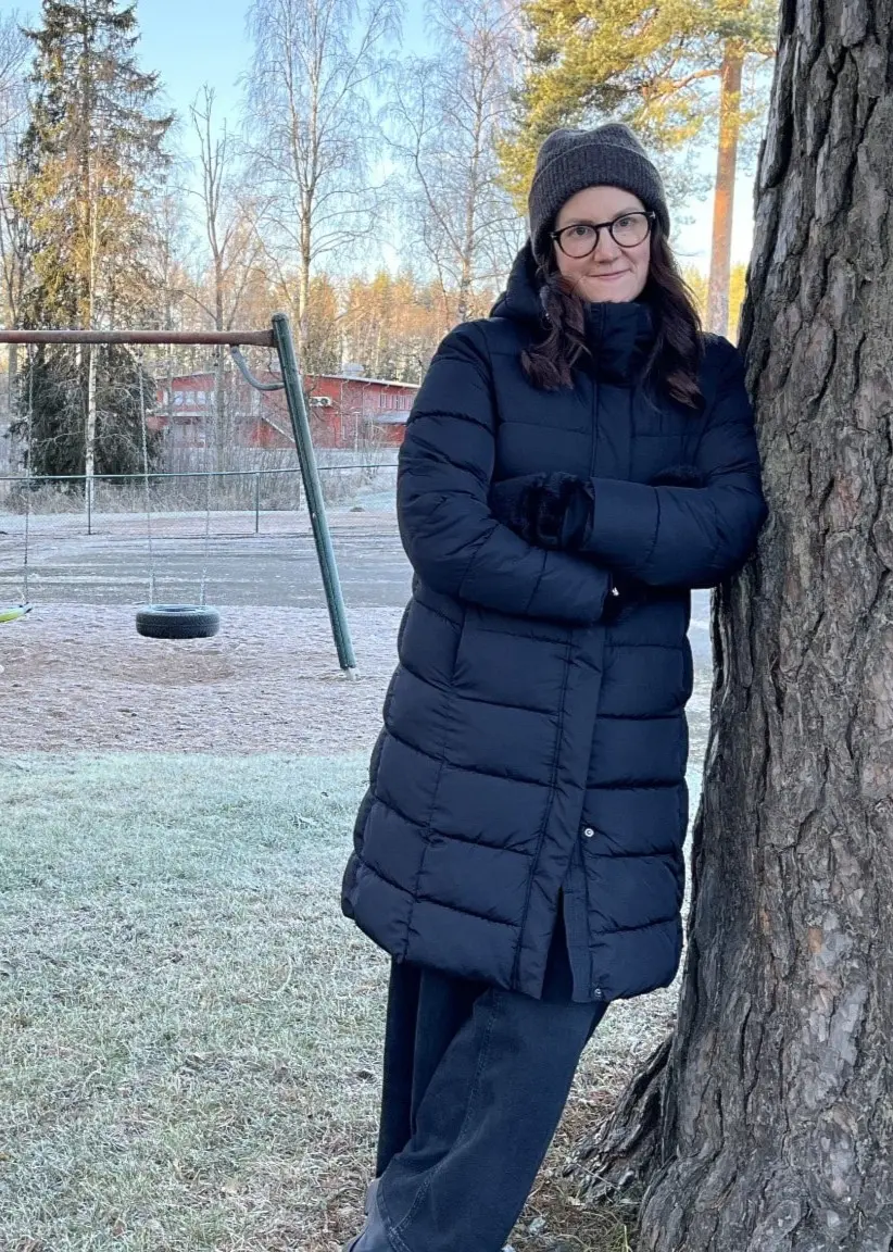 Matilda Hansson från Hofors står lutad mot ett träd i en kall utomhusmiljö, klädd i mörk vinterjacka och mössa. En tom lekplats med gungor syns i bakgrunden.