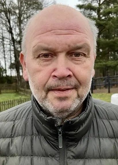 Lennart ”Kral” Andersson står utomhus framför en röd villa med vita knutar och en stapel av vita balar på en grusad gård. Han bär en grå vadderad jacka.