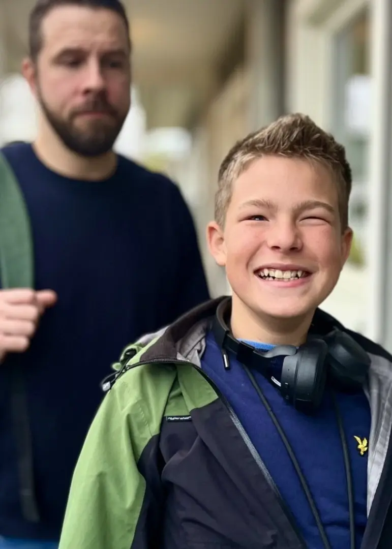 En man, identifierad som Martin Malmberg, står utomhus vid en husfasad med en grön axelväska. I förgrunden syns ett barn i jacka och hörlurar, båda på väg någonstans.