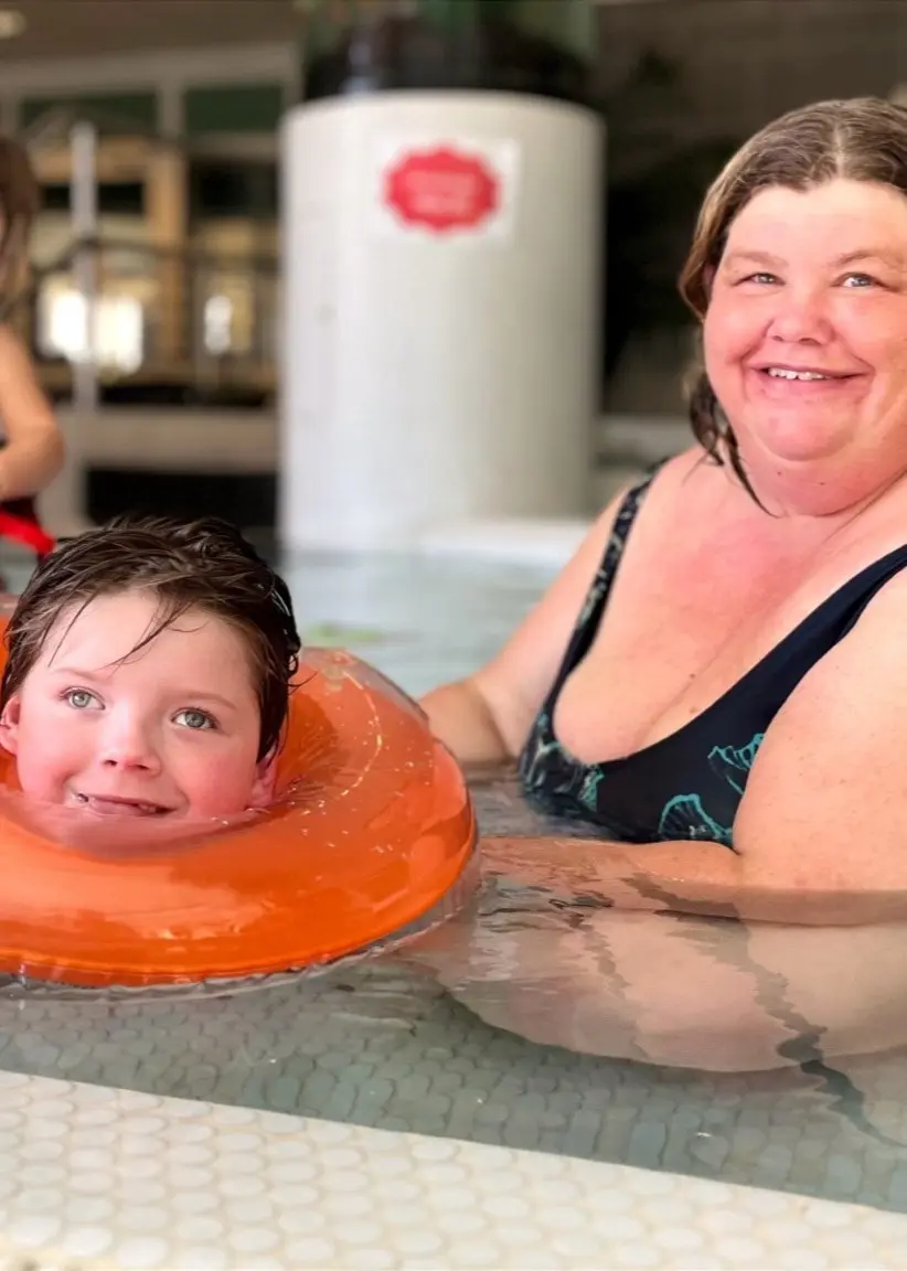 BojBritt och hennes mamma Susann Janhans sitter i en bassäng på Alfta Simhall, omgivna av vattenleksaker och andra besökare i bakgrunden.