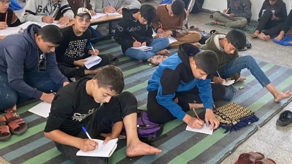 Barn sitter på en grön och svartrandig matta med sina skrivhäften.