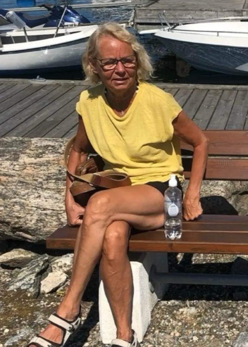 Gun-Britt sitter på en bänk vid en hamn i solen.