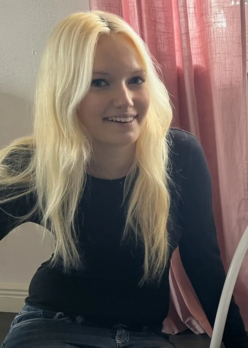 My Nyström sitter bredvid en babysitter där ett spädbarn ligger. Rummet har rosa gardiner och ett fönster med prydnadsföremål och växter.