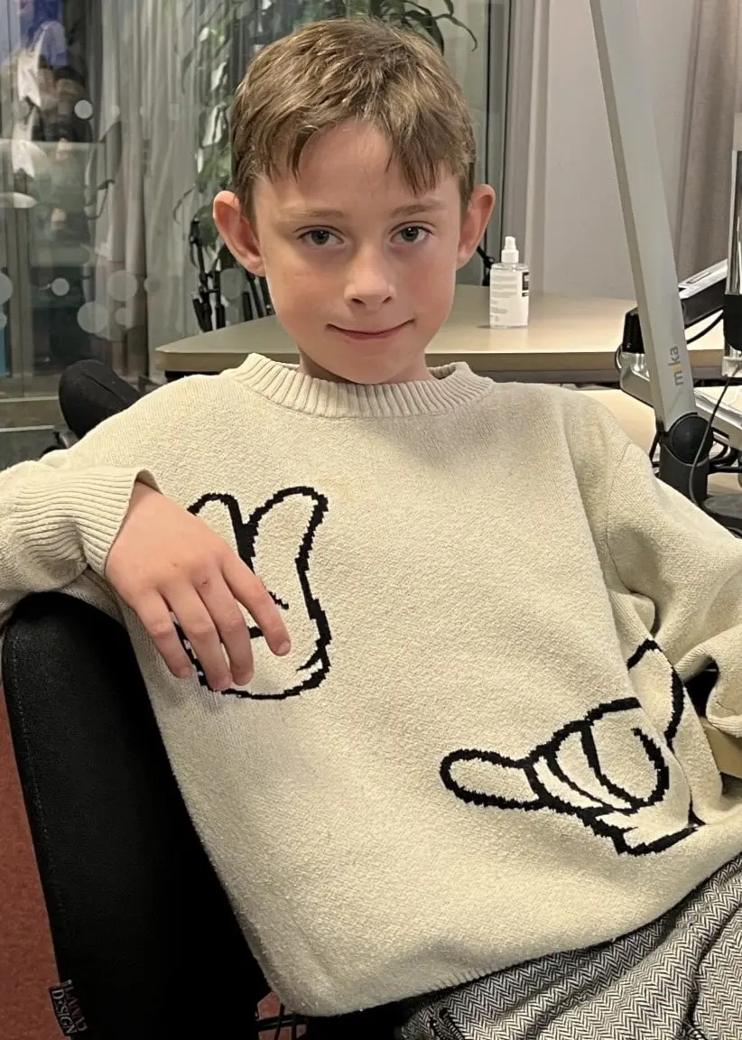 Zack Funksjö sitter i en radiostudio med modern utrustning. Han bär en stickad tröja med tecknade motiv och mönstrade byxor.