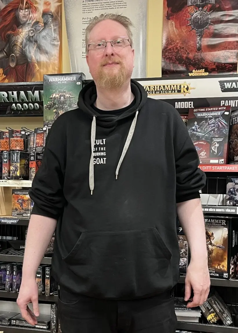 En man, identifierad som hobbybutiksinnehavaren Stig Rudeholm i Gävle, står framför hyllor fyllda med brädspel, figurspel och samlarprodukter i en hobbybutik.