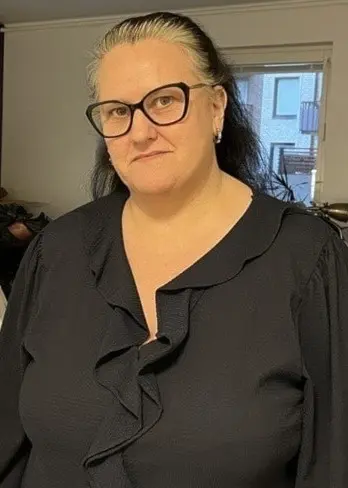 Christina står i ett vardagsrum fyllt med flyttlådor och möbler. Bakom henne syns stora fönster och en köksbänk.