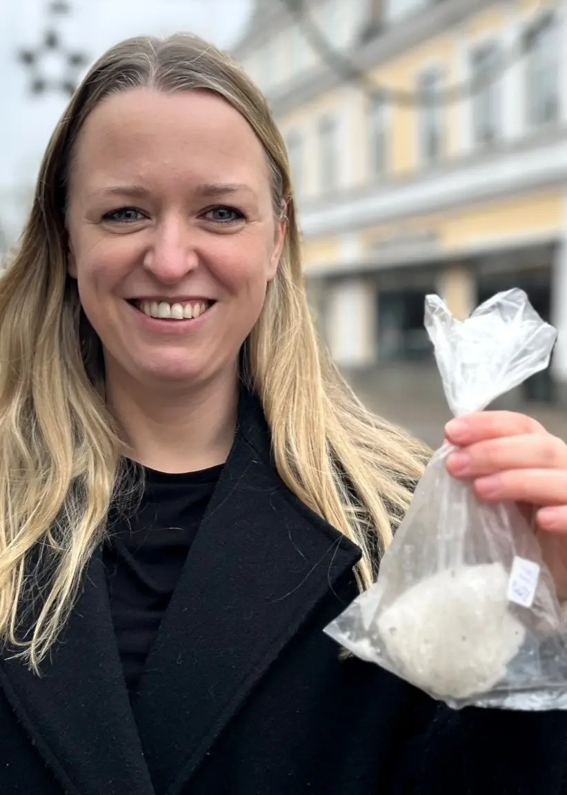Jonna Nyberg från Rottne håller upp en plastpåse med en snöboll på en gata med butiksfasader i bakgrunden. Hon sparade snöbollen i frysen år 2001 och den finns kvar än idag.