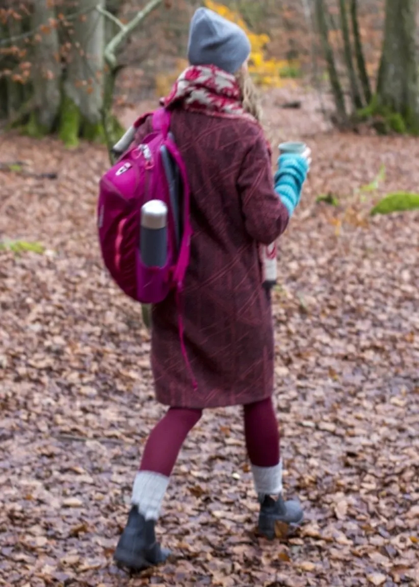 Kvinna i vinröda kläder med ryggstäck som går i ett höstlandskap.
