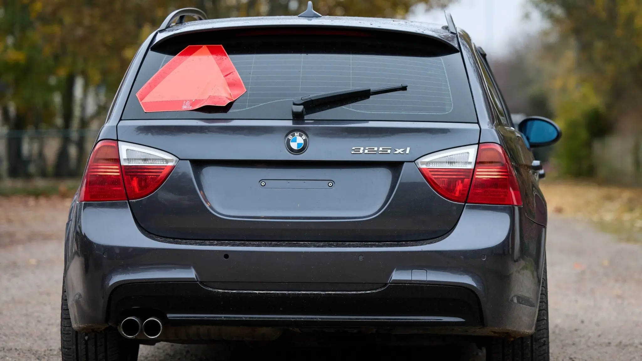 En grå BMW A-traktor med en tydlig röd varningstriangel på bakrutan står parkerad på en grusväg omgiven av höstliga träd. Bilden illustrerar nya regler för A-traktorer i Sverige.