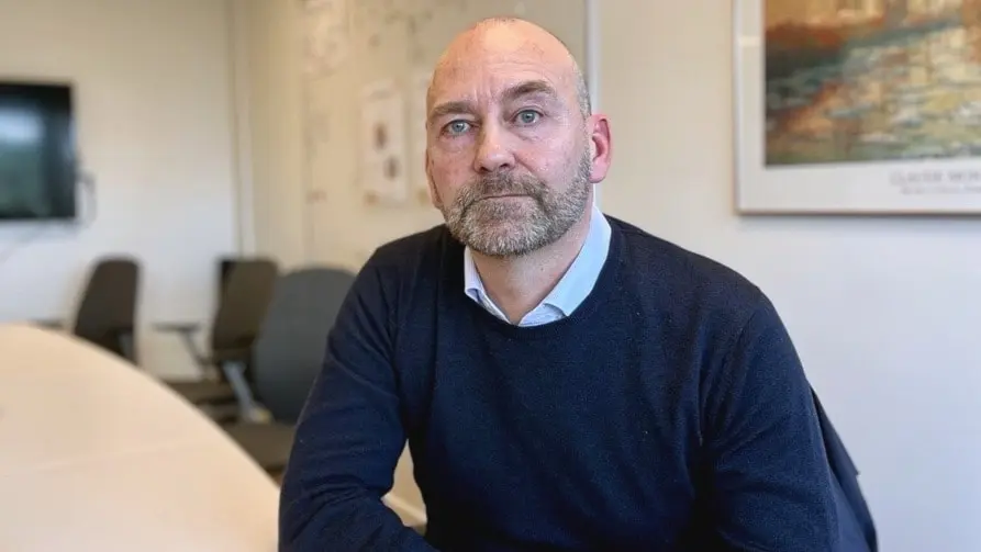 Marcus Walldén (M), ordförande för barn- och utbildningsnämnden, sitter vid ett konferensbord i ett kontorsrum med en vit tavla och en väggmålning i bakgrunden.