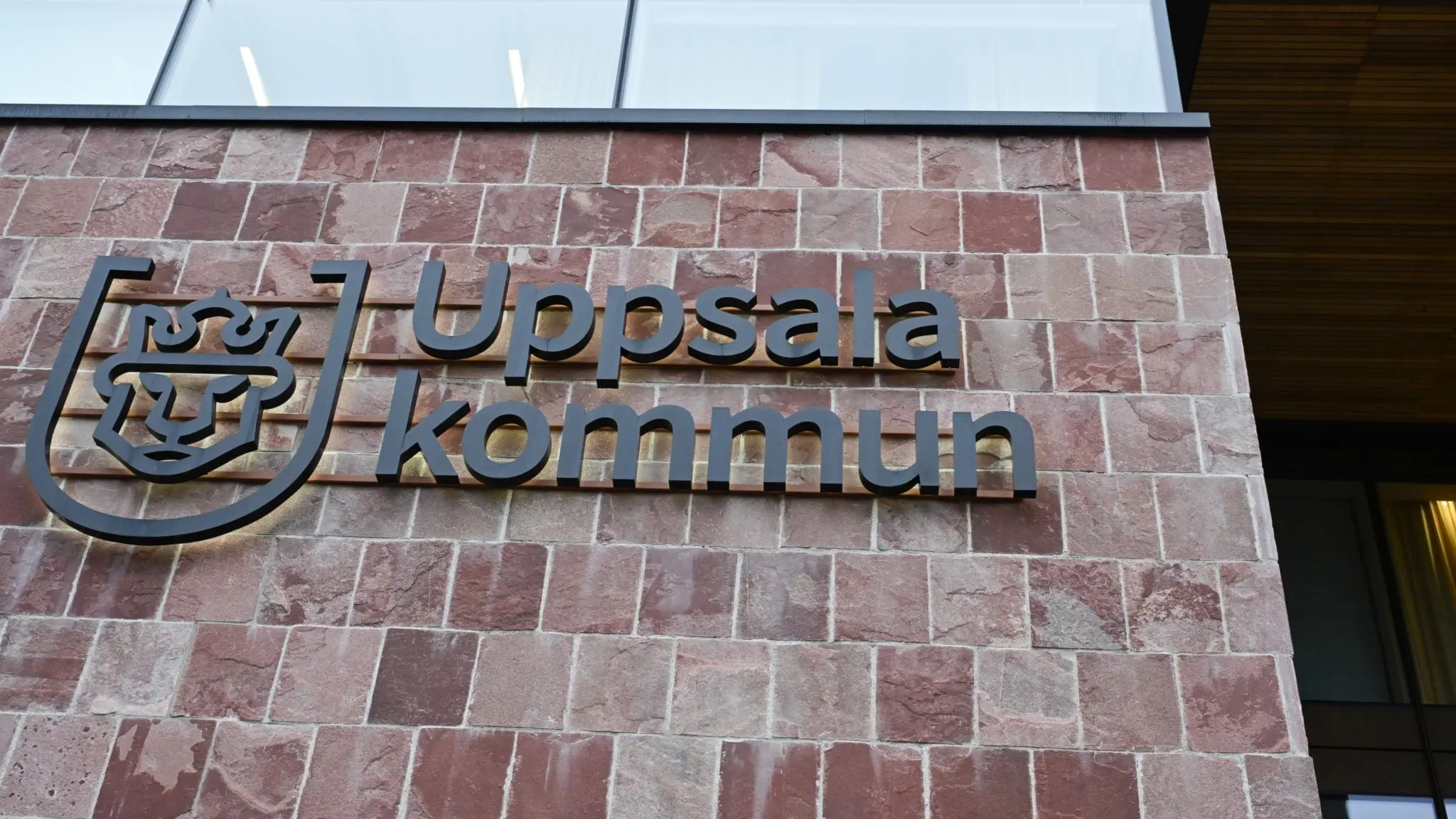 Fasad av en byggnad med Uppsala kommuns logotyp och text monterad på en röd stenmur, symboliserar lokal myndighet och administration.