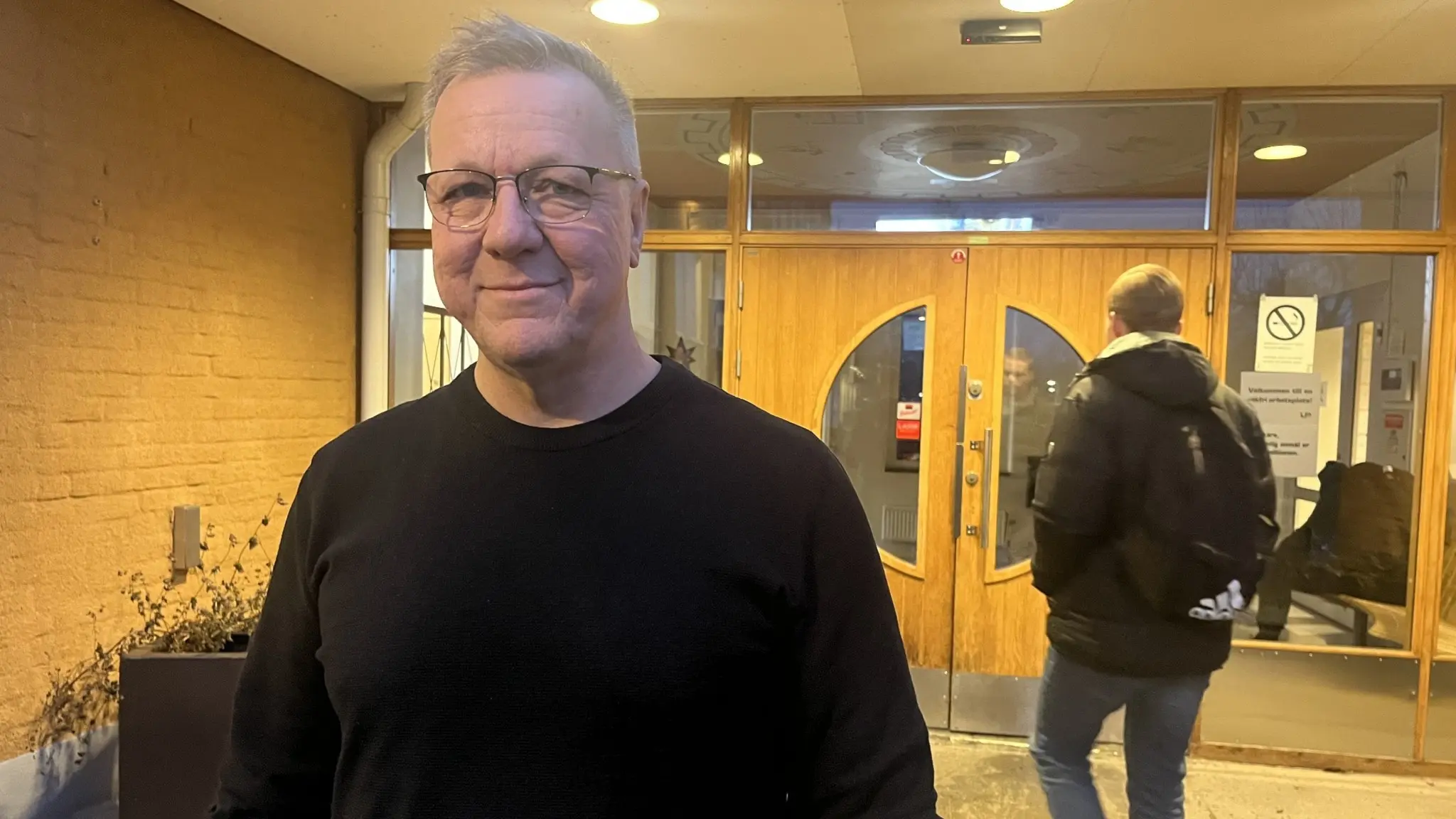 Jonas Jansson, skolledare vid Häggviks anpassade gymnasium i Sollentuna, står framför skolans entré med en annan person som går mot dörrarna i bakgrunden.