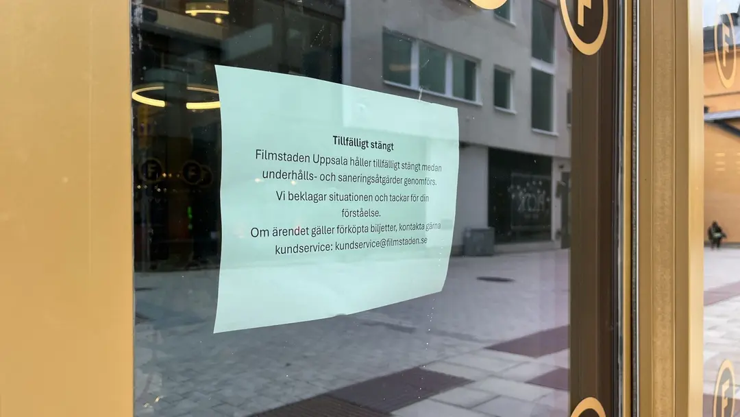 Ett anslag på en glasdörr vid Filmstaden Luxe i Uppsala informerar om tillfällig stängning på grund av upptäckta vägglöss. I en reflektion på dörren syns en gata med byggnader.
