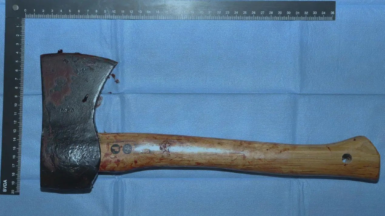 Blodig yxa fotograferad på blå bakgrund med en linjal för att visa storlek. Yxan misstänks vara ett mordvapen och används som bevis i en brottsutredning.