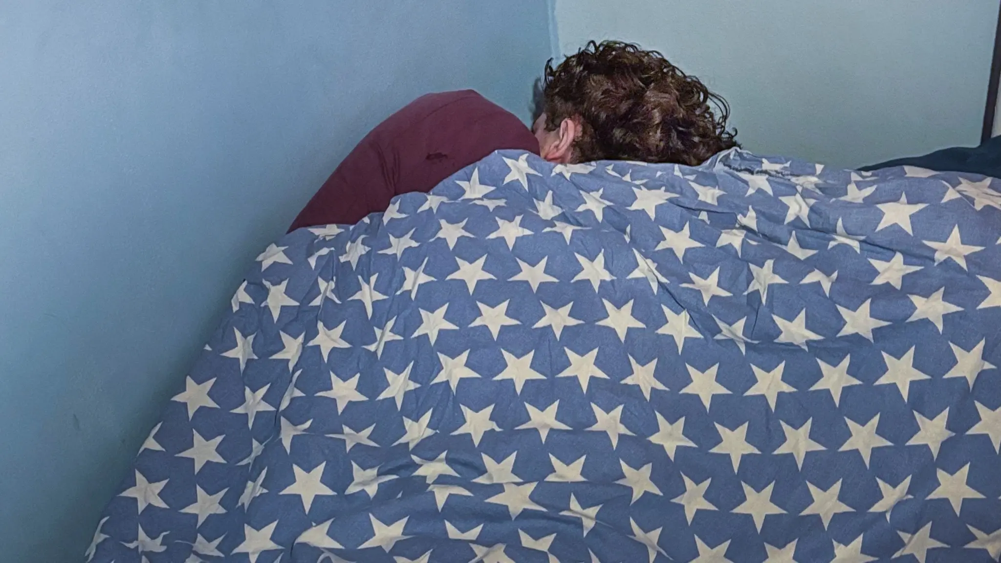 En ung person som ligger under täcket och sover.