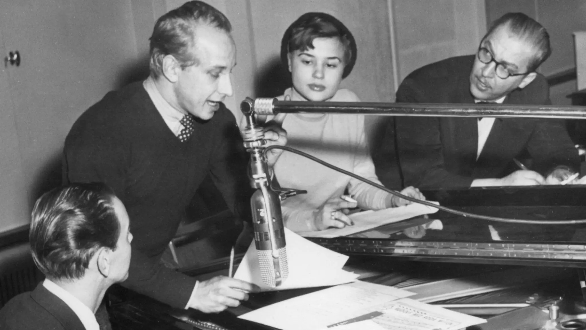 Charles Norman, Gunnar Wersén, Harriet Andersson och Arne Källerud sitter runt en pianoflygel. I mitten syns en mikrofon på stativ.