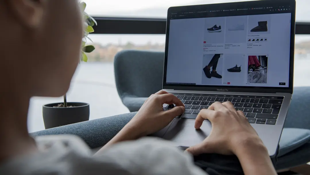 En ungdom sitter vid en laptop och surfar på e-handelssidor med skoval. Bilden illustrerar miljövänlig julshopping via internet, med fokus på digital konsumtion och hållbarhet.