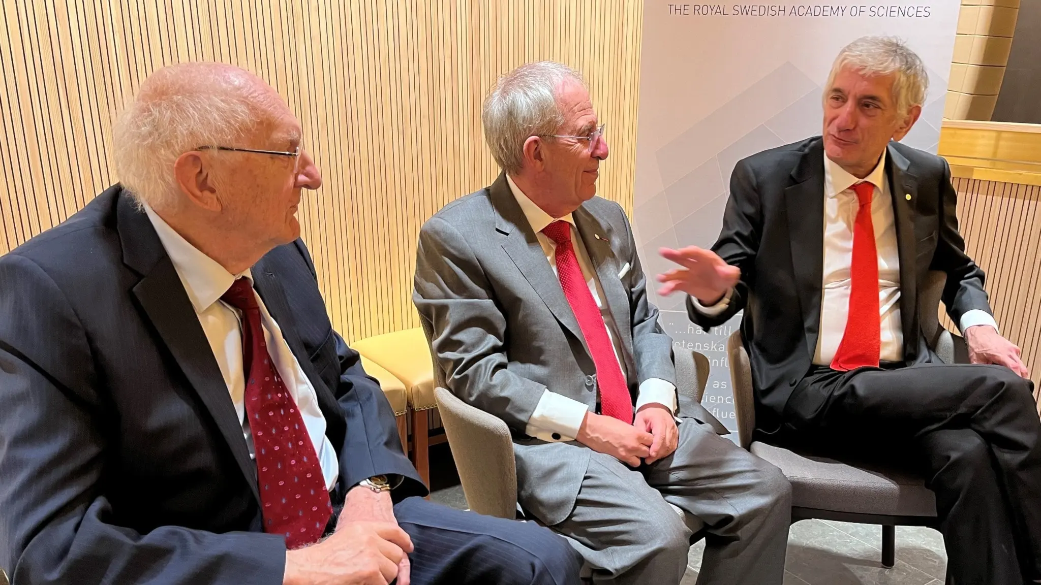 John Clarke, Michel Devoret och John Martinis sitter bredvid varann i fåtöljer. martinis gestikulerar, de två andra lyssnar på honom.