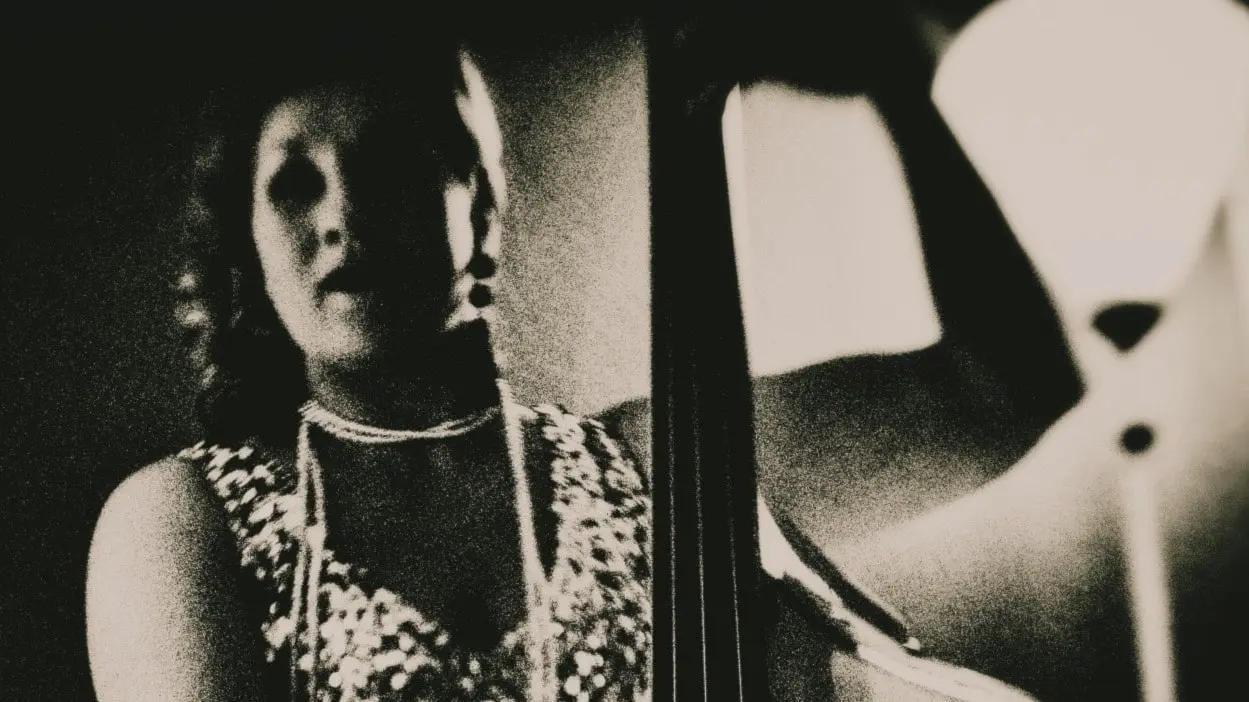 En kvinna i pärlhalsband och spetsklänning spelar kontrabas