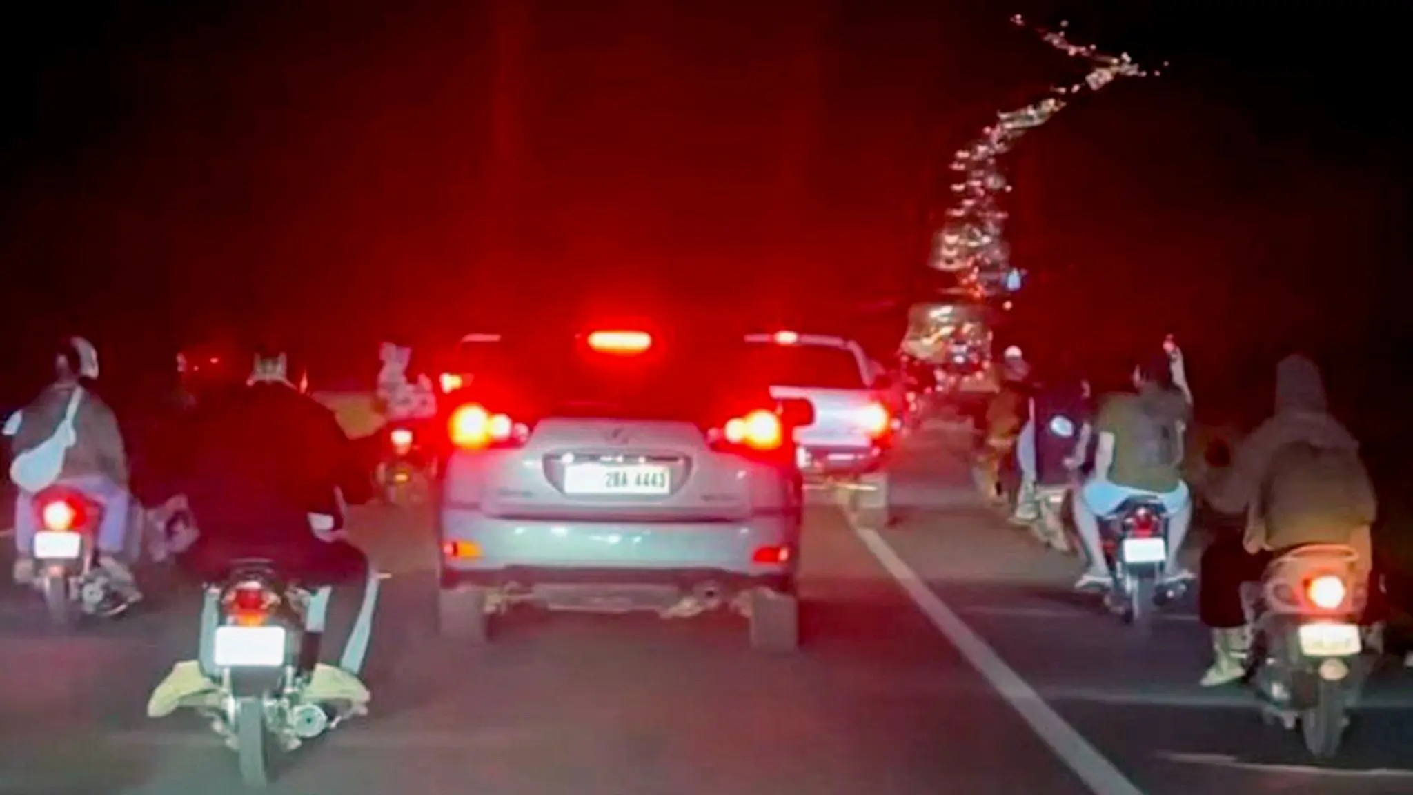 Människor ses evakuera på motorcyklar och i bilar längs en mörk väg i Kambodja.