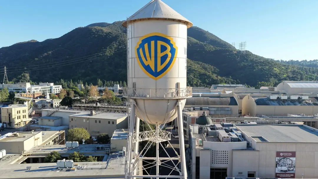 Warner Bros. ikoniska vattentorn med företagets logotyp syns från ovan, omgiven av studiolokaler och berg i bakgrunden. Bilden representerar en affär mellan Netflix och Warner Bros.