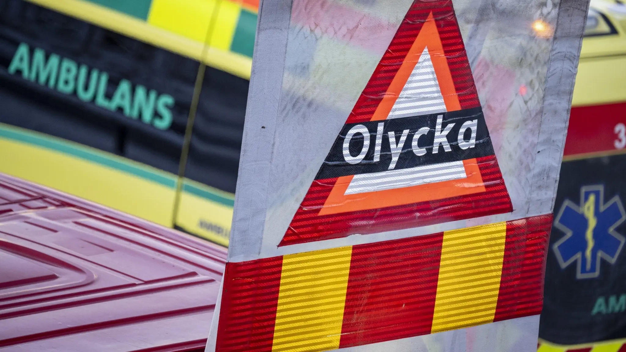 En varningsskylt med texten 'Olycka' framför ambulans och räddningstjänstfordon.