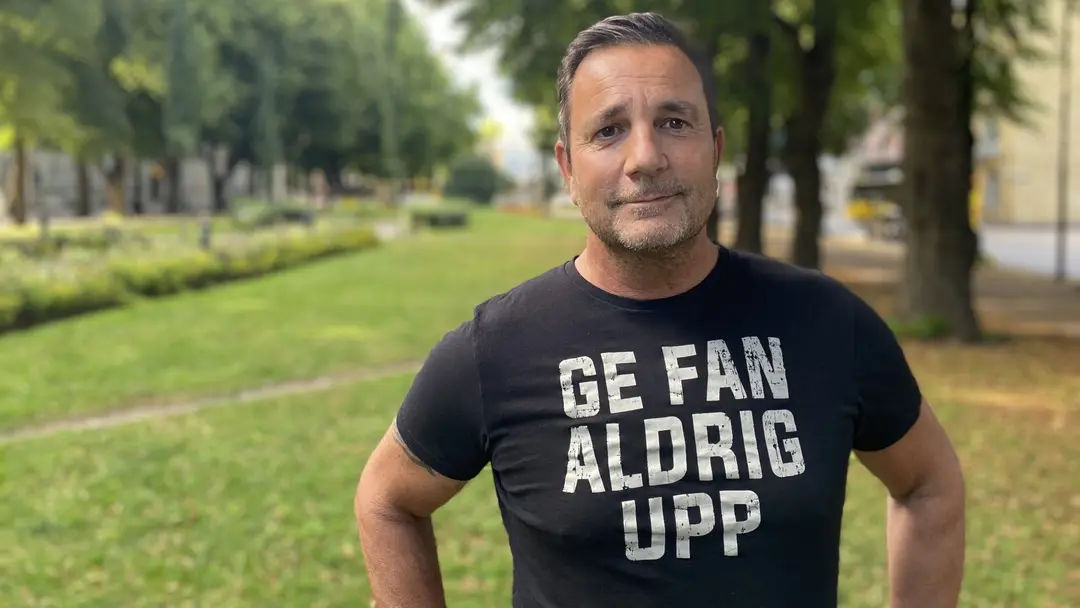 En man tittar in i kameran med grönska i bakgrunden