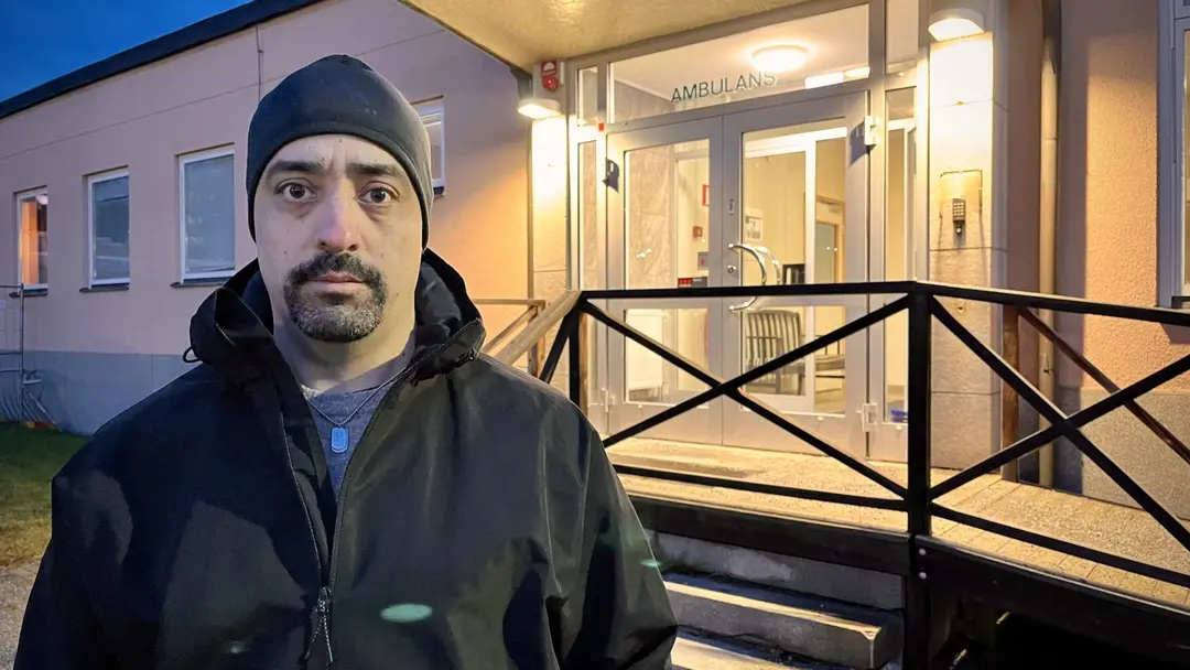 Ambulanssjuksköterskan Anders Lindkvist står utomhus framför en byggnad med ramp och upplyst entré i bakgrunden, iklädd mörk jacka och mössa.