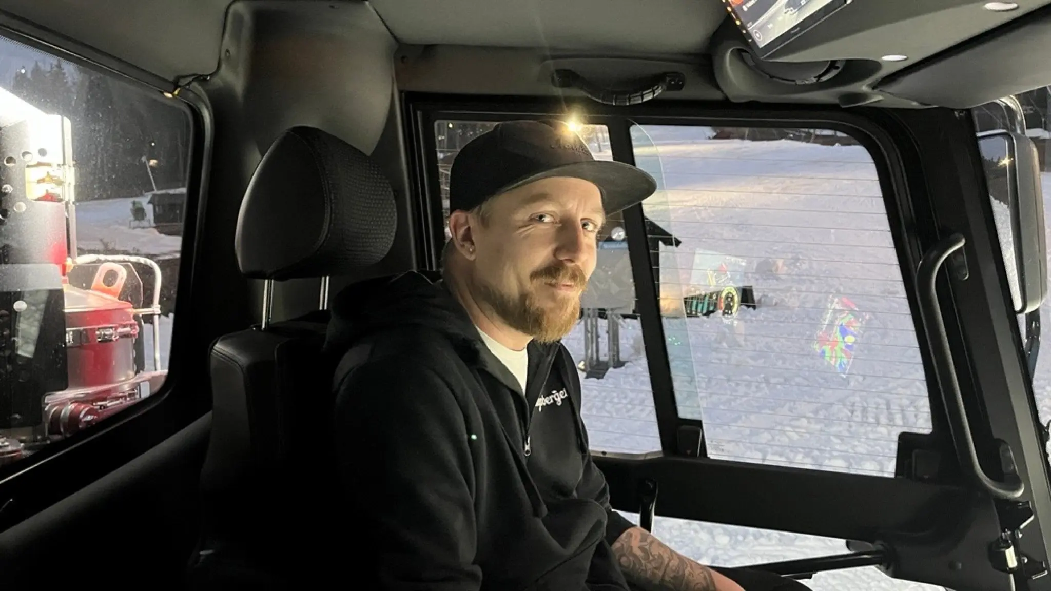 Markus Alanärä sitter vid förarplatsen i en modern pistmaskin, omgiven av stora fönster som visar en skidanläggning utanför. Han arbetar med preparering av skidbackar.