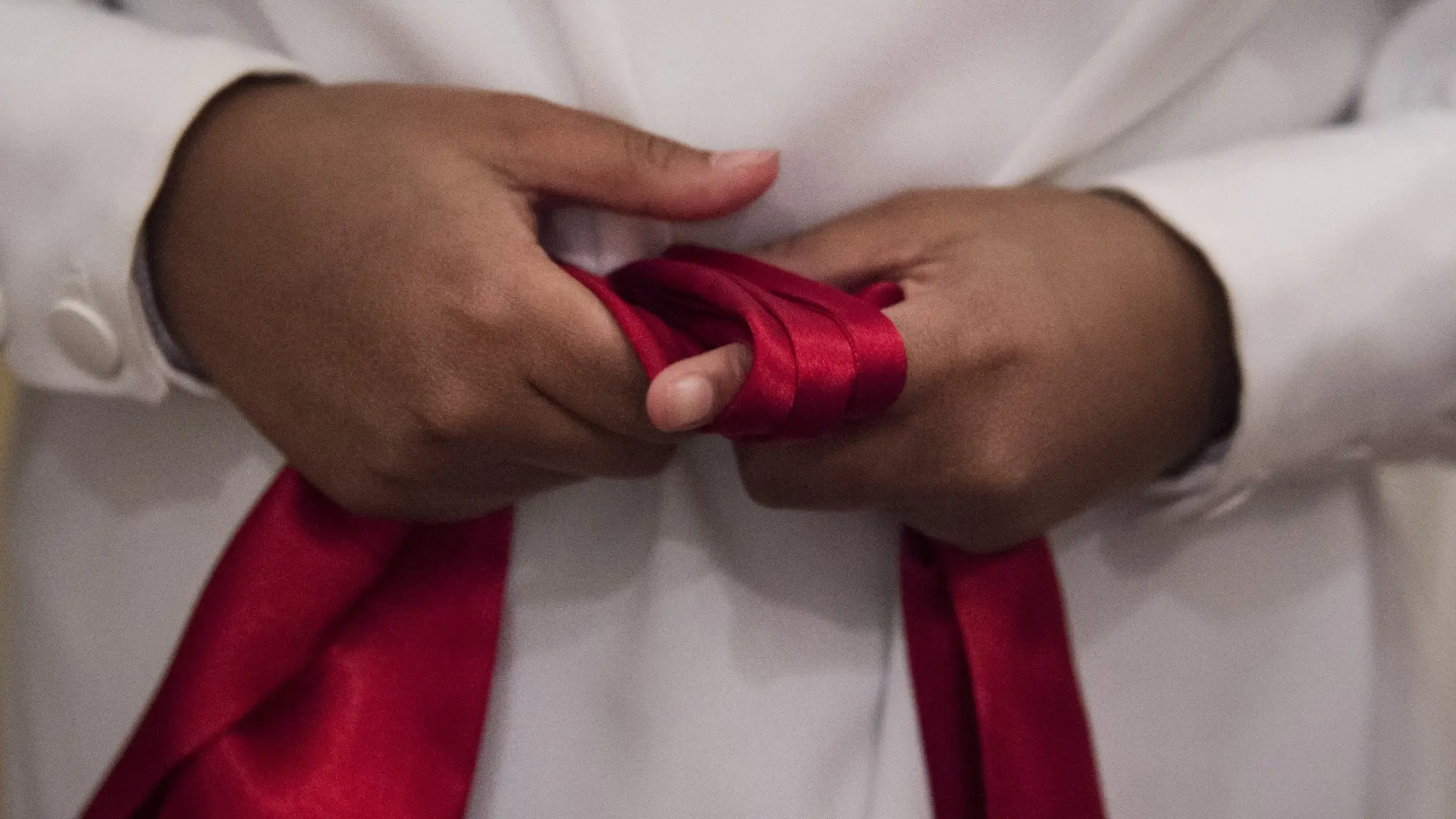 En person klädd i vit luciaklänning knyter ett rött sidenband runt midjan.