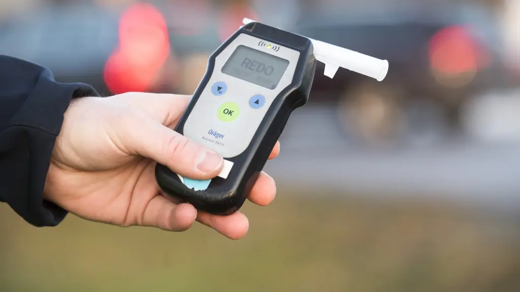 En polis håller i ett blåsinstrument för nykterhetskontroll. Bakgrunden visar en oskarp väg med passerande bilar i trafik. Bilden illustrerar trafikkontroll och alkoholtest.