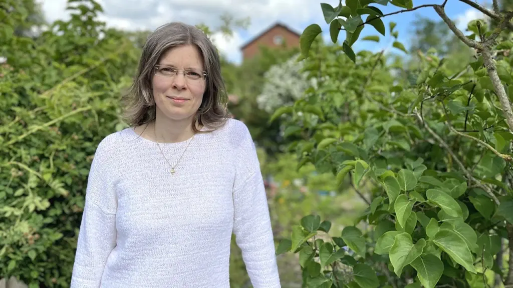 Jasmine Lindsten, ordförande för logopedförbundet i Skåne, står utomhus bland grönskande träd och buskar. Hon har på sig en ljus tröja och himlen är delvis blå med några moln.