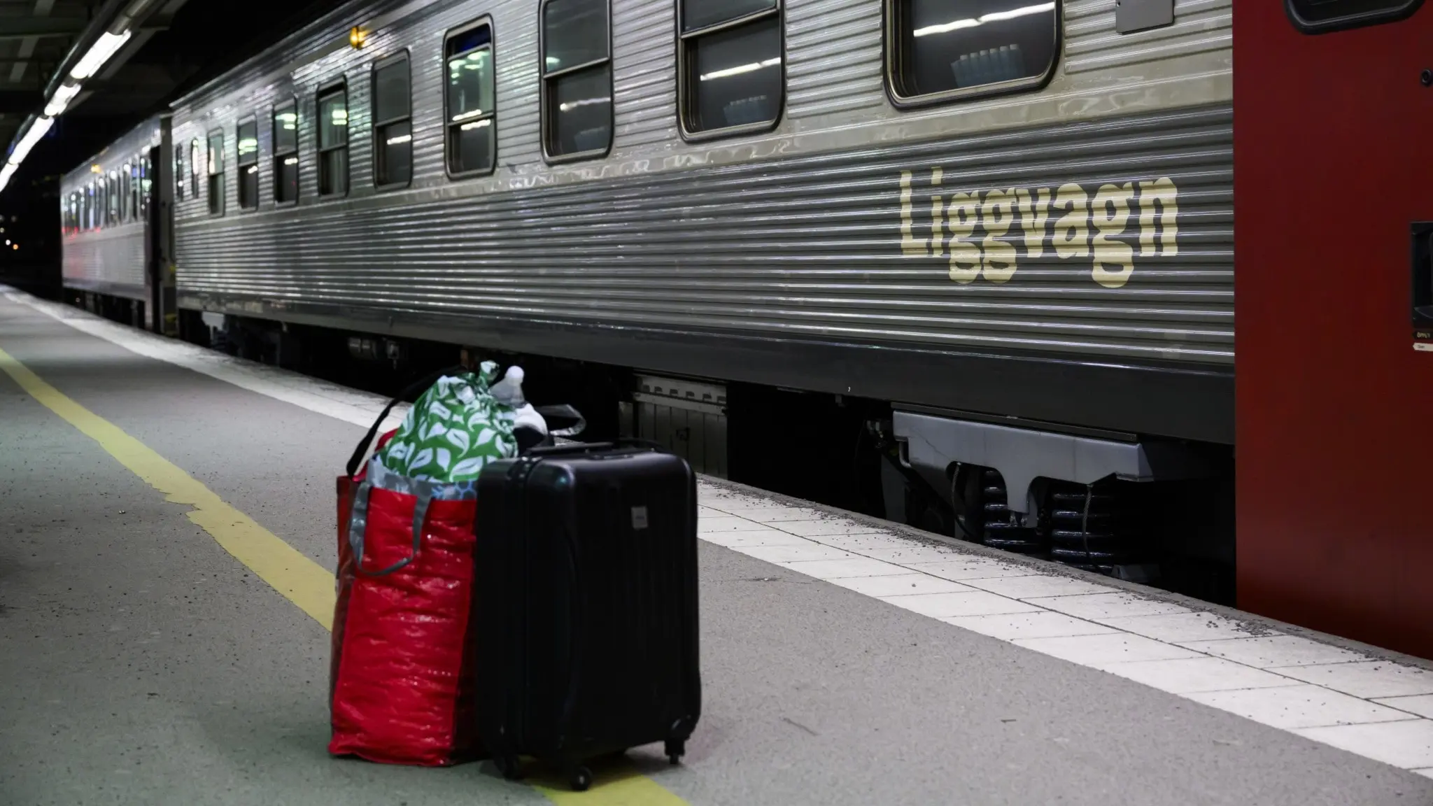 Ett nattåg står vid perrongen på Stockholms centralstation. Framför tåget syns två resväskor, en svart och en röd, samt en grön påse. Perrongen är tom och upplyst av taklampor.