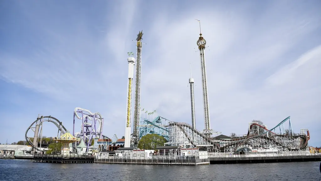 Vy över Gröna Lund med flera höga attraktioner, inklusive berg- och dalbanor och fritt fall-torn, beläget vid vattnet under en klar himmel.