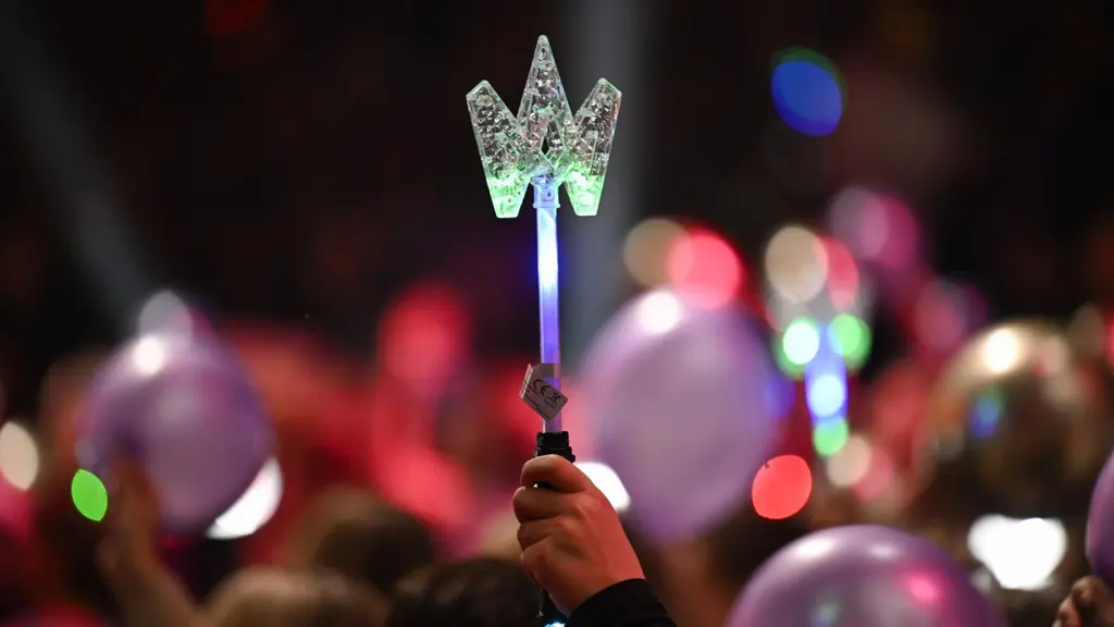 Publik på Melodifestivalen med en lysande stjärnformad stav i förgrunden, omgiven av färgglada ljuseffekter och ballonger i en festlig atmosfär.