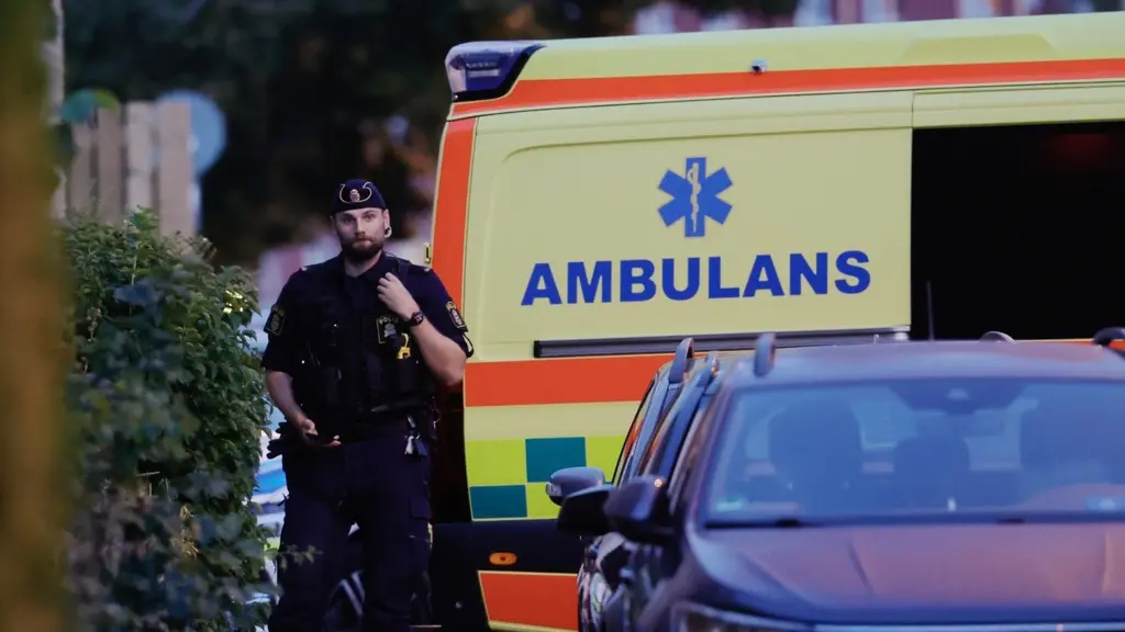 En polis står bredvid en gul ambulans med blå text på Hisingen. Bilden visar en utryckning med flera fordon, inklusive en bil i förgrunden.