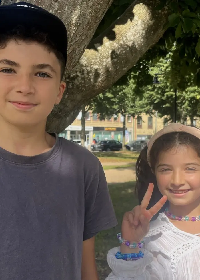 Hadi Shamie och Thalia Shamie står vid ett träd i en park. Barnen ler mot kameran, och flickan gör segertecken.