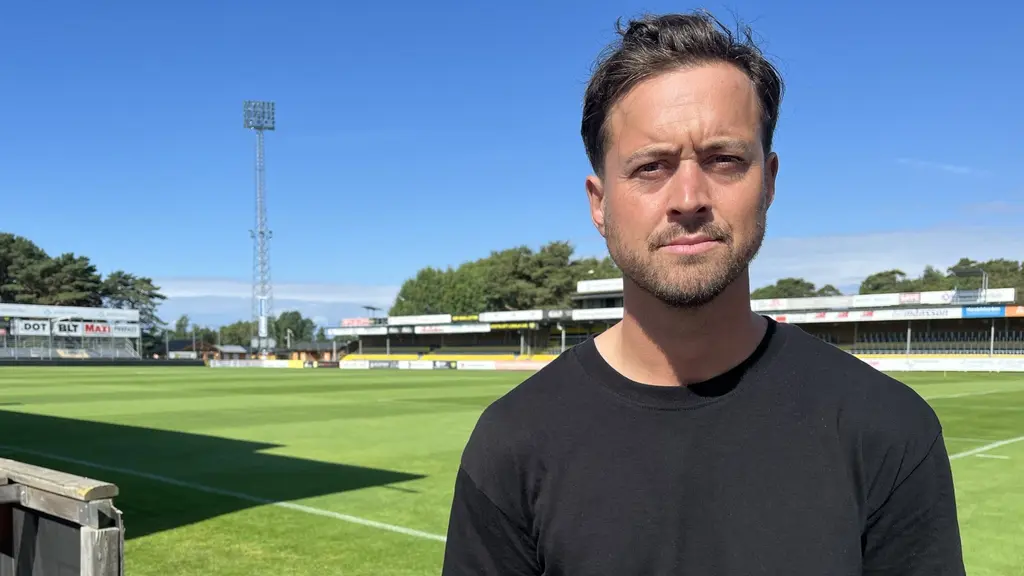 Mjällby AIFs klubbchef Jacob Lennartsson står vid en fotbollsplan i solsken.