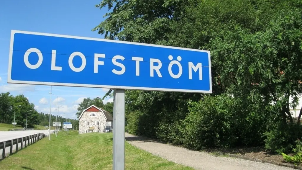 Vägskylt med texten Olofström vid infarten till orten, omgiven av grönska och landsväg.