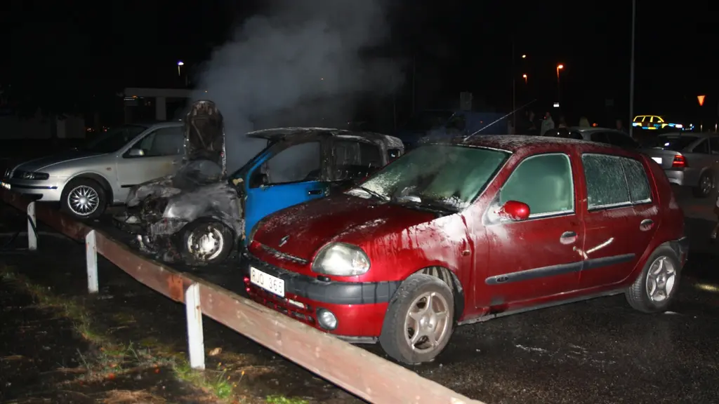 Tre parkerade bilar, det ryker ur den mittersta bilen som är brandskadad och den närmaste bilen är också lite bränd. 