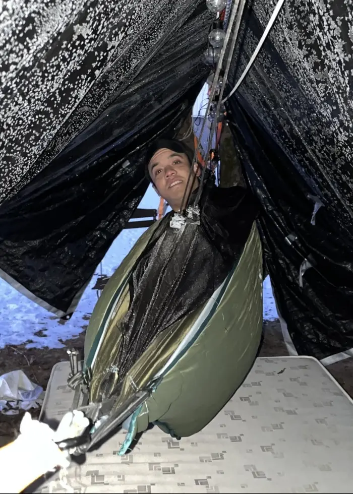 En person, identifierad som Sam Johnsson, ligger i en hängmatta under ett tält. Snö täcker marken och tältet verkar vara uppsatt i en kylig utomhusmiljö.