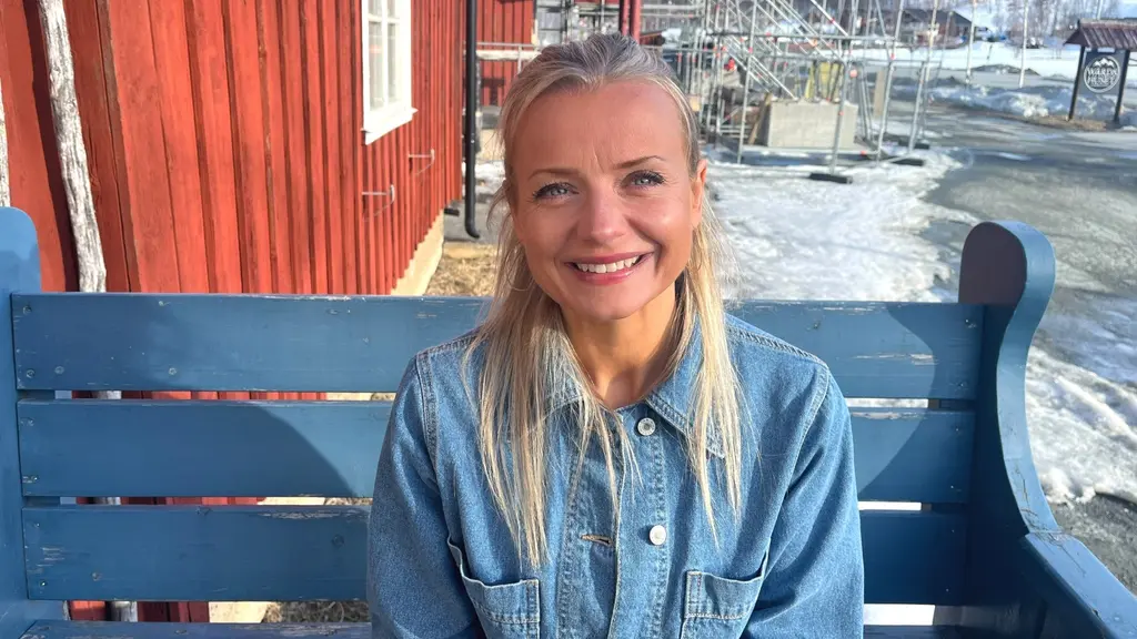 Johanna Forsberg sitter på en blå bänk framför en röd byggnad i Hemavan. Hon har långt hår och bär en jeansjacka.