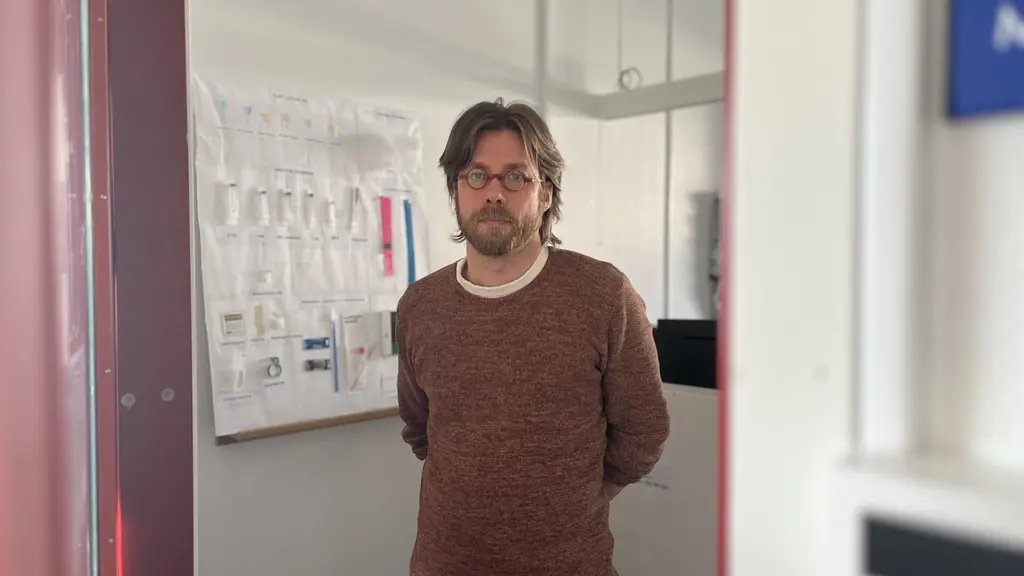 Jonas Stenberg befinner sig i lokalen där narkomaner får nya sprutor. Han bär en brun tröja. På väggen hänger sprutor.