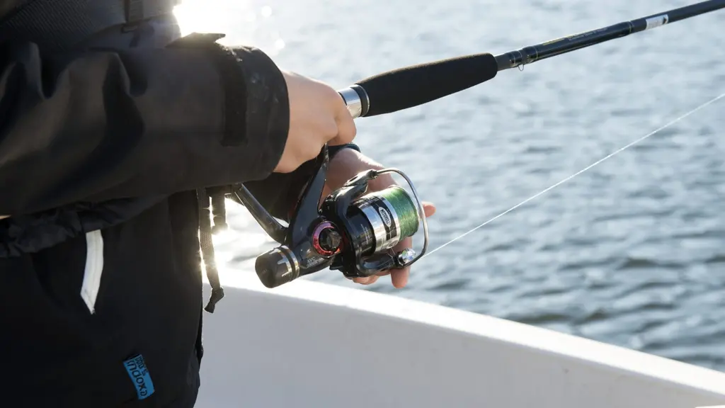 En person klädd i mörk jacka håller i ett fiskespö på en båt, med fokus på rullen och en glittrande vattenyta i bakgrunden.