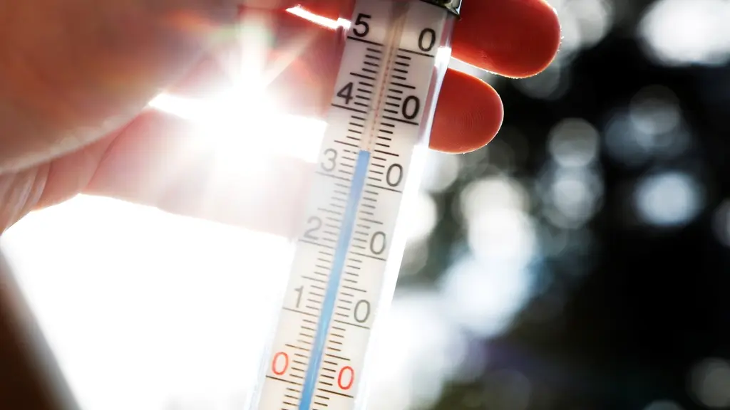 Hand håller termometer som visar över 30 grader, bilden tagen i motljus mot sol.